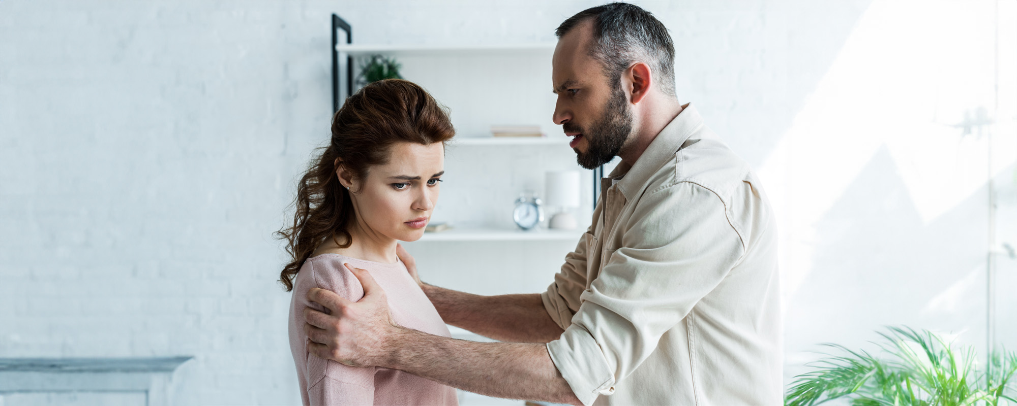 angry man touching offended brunette woman at home