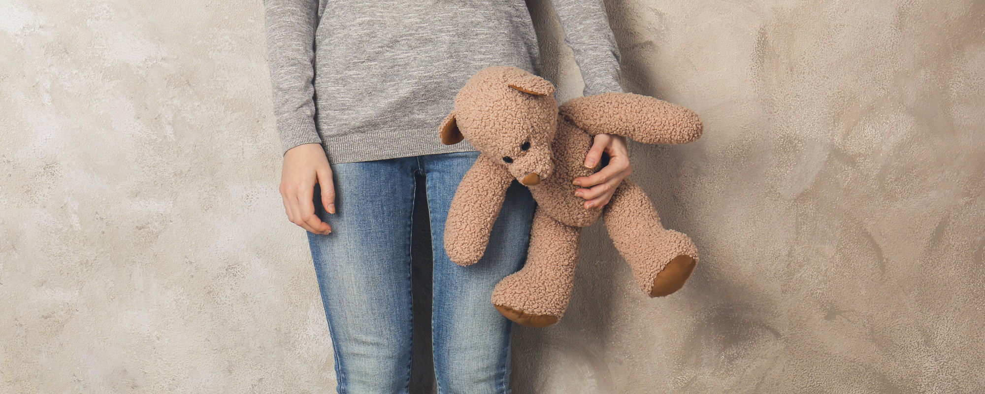 little girl standing with toy bear on color wall