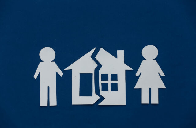 The concept of separation of property, divorce. Half-cut paper house and figures of man and woman on classic blue background