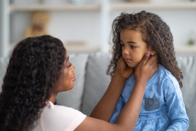 Family misunderstanding, childhood problems concept. Young black mother comforting her sad offended daughter after quarrel at home. African American woman calming down her child