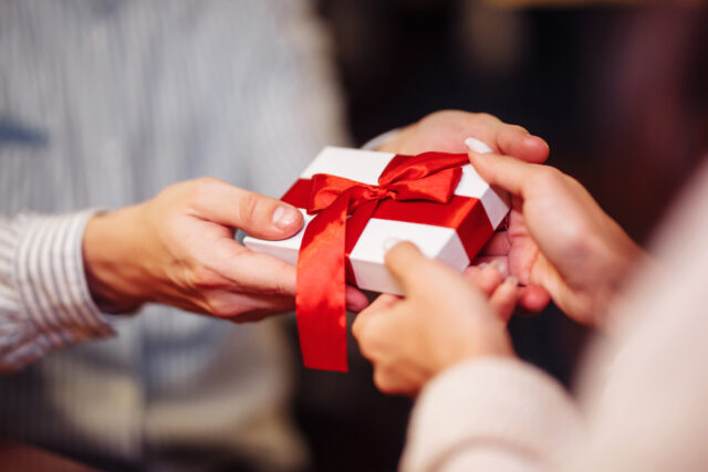 Valentine's Day concept. Close shot of man's and woman's hands presenting gifts to each other at a cafe. A young loving couple celebrating in the restaurant. New normal, winter holidays