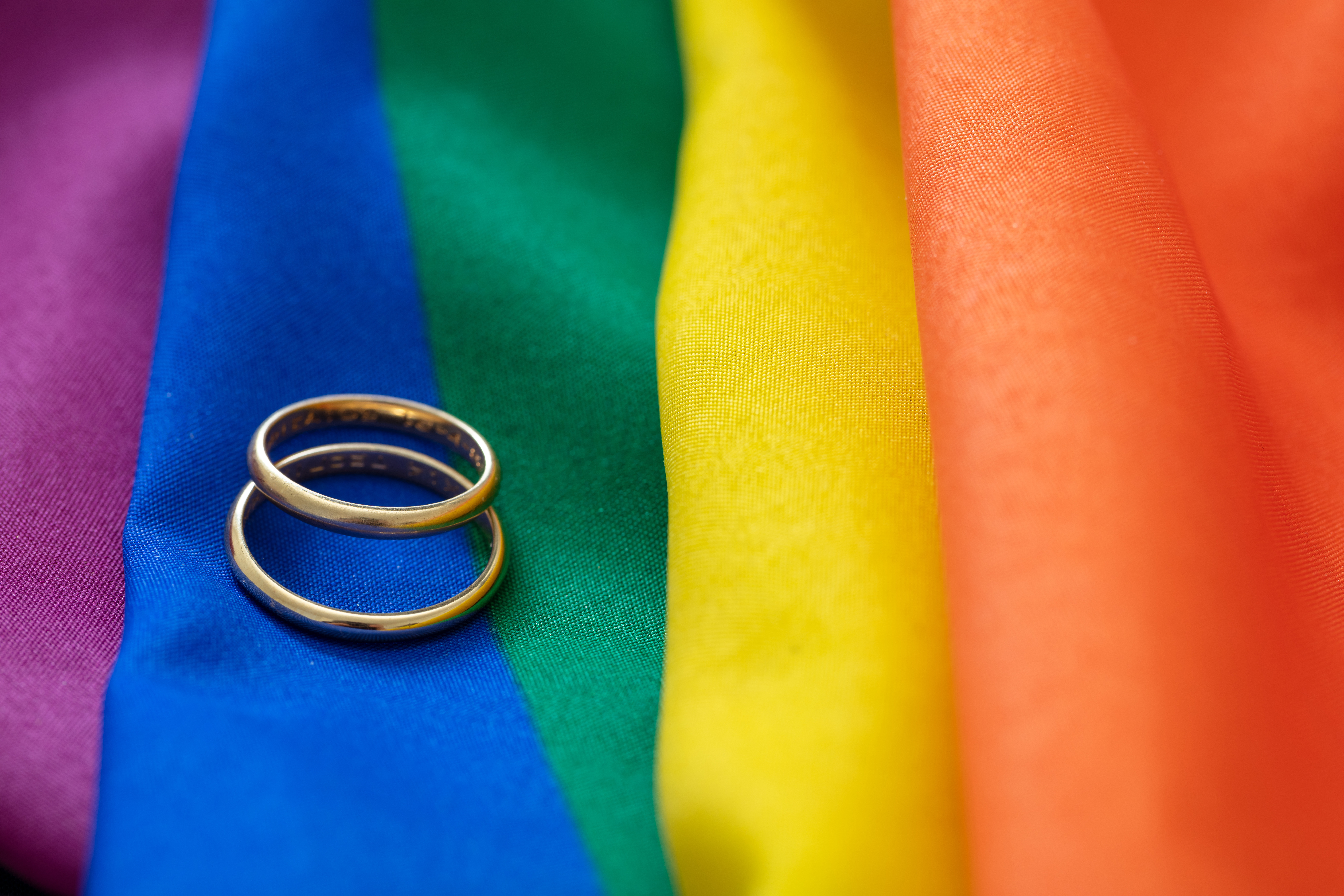 LGBT Gay marriage. Pair of golden rings on rainbow color textile with creases, close up view. Copy space.